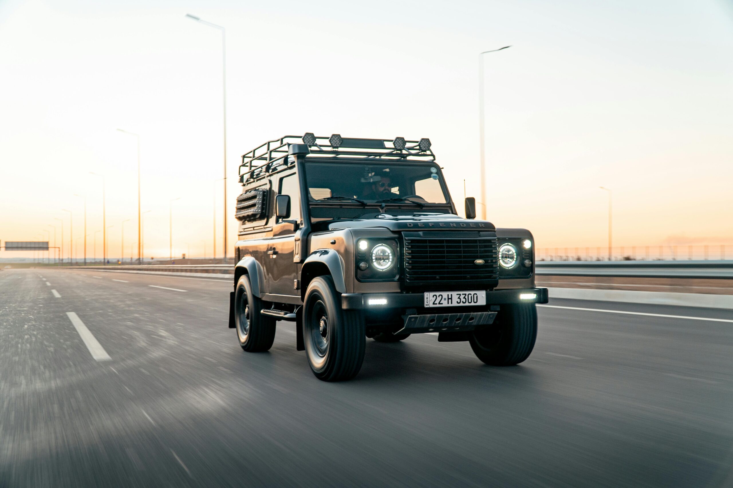 A Land Rover Defender cruises on a highway in Erbil during sunset, capturing speed and adventure.